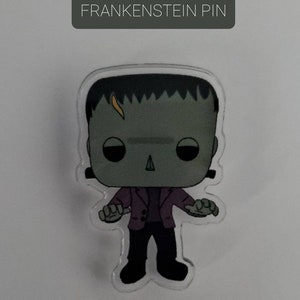 May include: A green Frankenstein character with black hair and a purple jacket. The character is wearing black pants and black shoes. The character is a pin with a clear background. The text "FRANKENSTEIN PIN" is at the top of the image.