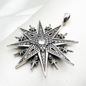 May include: A silver pendant in the shape of a large, eight-pointed star with a smaller star at each point. The star is covered in small, clear crystals.