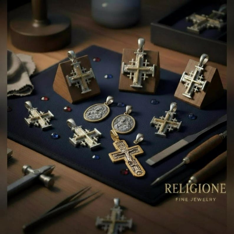 Puede incluir: Una colecci&oacute;n de colgantes de cruz y medallones religiosos circulares en metal plateado y dorado sobre una alfombrilla azul oscuro. Varias cruces est&aacute;n montadas en bloques de madera. Se ven herramientas de joyer&iacute;a como una lima.