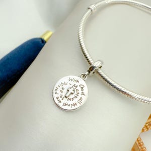 Op de afbeelding: Zilveren armband met een ronde bedel met de tekst "Met God is alles mogelijk - Mattheüs 19:26" en een klein kruis.