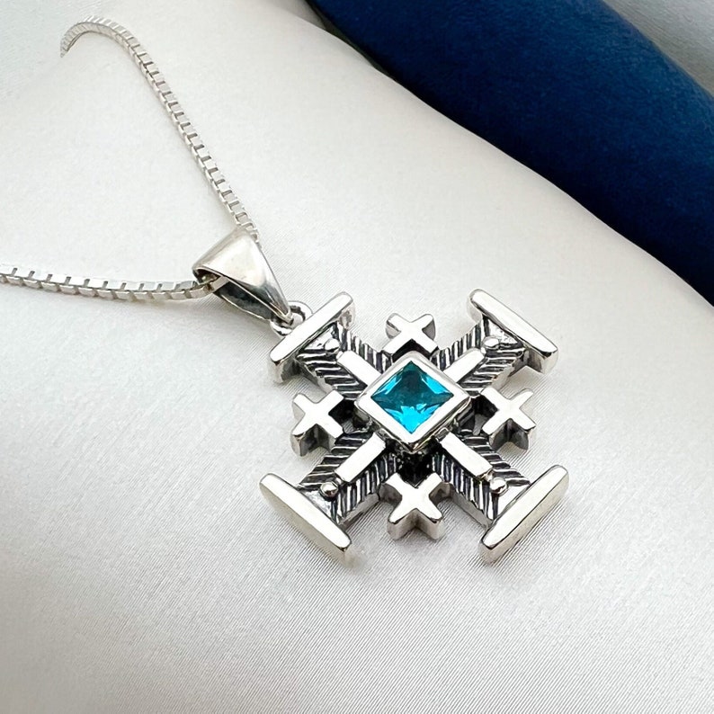 Pu&ograve; includere: Una collana d'argento con un ciondolo che presenta un design a croce dettagliato con una pietra preziosa blu al centro.