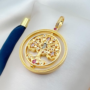 Può includere: Un ciondolo per collana in oro con un designo dettagliato di albero della vita con pietre preziose colorate. Il ciondolo è rotondo e ha una funzione di rotazione.