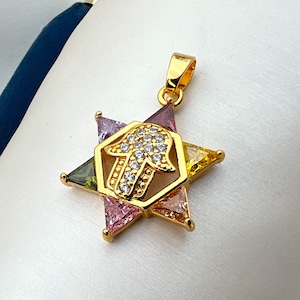 May include: A gold pendant featuring a Hamsa hand charm surrounded by a six-pointed star with colourful gemstones. The star is made up of six triangular sections with different coloured gemstones: green, pink, yellow, and red.