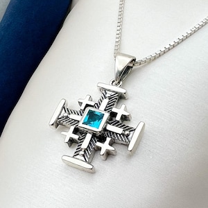 May include: A silver pendant necklace featuring a blue gemstone set in a detailed cross design.