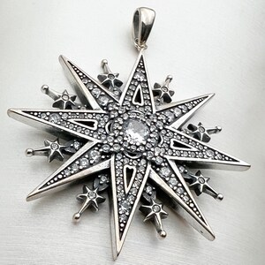 May include: A silver pendant in the shape of a eight-pointed star with a large clear crystal in the center. The star is decorated with smaller crystals around the edges.