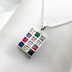 Può includere: Una collana d'argento con un ciondolo di forma quadrata con 12 pietre preziose colorate. Il ciondolo è in argento e ha una finitura lucida.