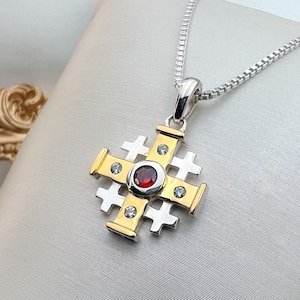 May include: A silver and gold pendant necklace with a red gemstone and white gemstones in the center of a cross design.