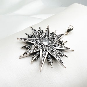 May include: A silver pendant in the shape of a eight-pointed star with a clear crystal in the center. The star is decorated with smaller crystals around the edges.