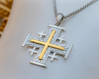 May include: Silver-tone Jerusalem cross pendant with a gold-colored cross in the center. The pendant hangs from a silver chain. The cross features ornate detailing and is displayed against a white background.