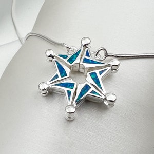 May include: A silver pendant necklace featuring a five-pointed star with blue and green opal inlay. The star is open in the center and has a hinged design.