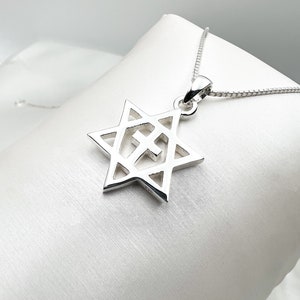 May include: A silver pendant necklace featuring a Star of David with a cross inside. The pendant is on a silver chain.