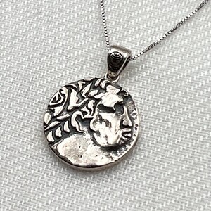 Può includere: Collana d'argento con un ciondolo rotondo che presenta un profilo dettagliato di un uomo con una corona di alloro. Il ciondolo è attaccato a una catena d'argento.
