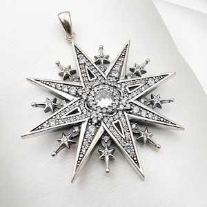 May include: A silver pendant in the shape of a star with a large clear crystal in the center. The star is surrounded by smaller crystals.