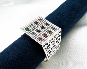 Op de afbeelding: Een zilveren ring met een vierkante bovenkant met een raster van 12 gekleurde edelstenen. De ringband is gegraveerd met Hebreeuwse tekst.