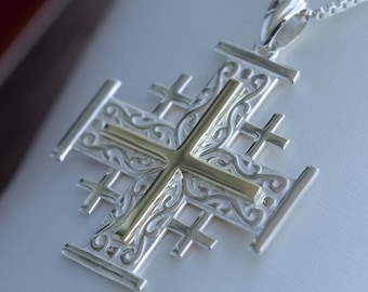 May include: A silver pendant necklace featuring a Jerusalem cross design with a gold-colored cross in the center. The pendant has an ornate, detailed pattern and is suspended from a silver chain.