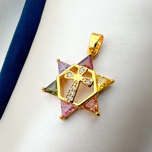 May include: Gold-tone pendant featuring a cross design with clear crystals inside a hexagonal frame, set within a multi-colored starburst of triangular gemstones. The pendant has a loop for a chain.