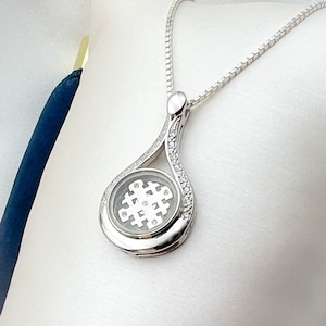 Puede incluir: Un collar de plata con un colgante en forma de lágrima. El colgante está adornado con pequeñas piedras transparentes y presenta un diseño circular con una piedra transparente más pequeña en el centro.
