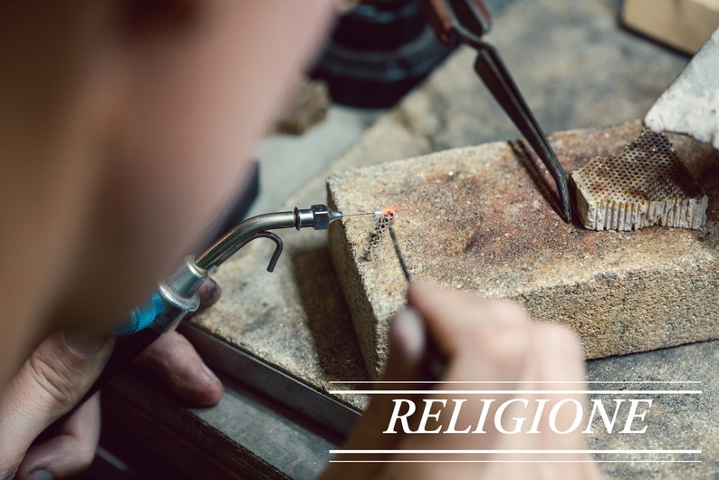 Pu&ograve; includere: Primo piano di una persona che usa un cannello per riscaldare un gioiello di metallo. Il metallo &egrave; tenuto in posizione con delle pinzette. La parola "RELIGIONE" &egrave; visibile nell'angolo in basso a destra dell'immagine.