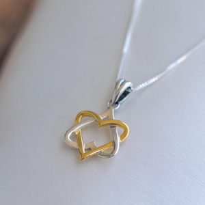 May include: A silver necklace with a pendant featuring a gold and silver heart design. The pendant is a combination of two interlocking hearts, one gold and one silver, suspended from a delicate silver chain. The jewelry is displayed on a white surface.