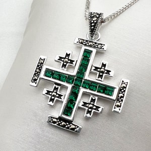 May include: A silver pendant necklace with a green crystal Jerusalem cross design. The cross is made of multiple smaller crosses with green crystals in the center of each.