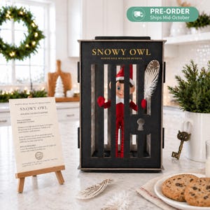 May include: A black wooden cage with vertical bars containing a small elf doll wearing a red suit and hat. The cage is labeled SNOWY OWL NORTH POLE WILDLIFE RESERVE and features a keyhole. A white feather and a printed report on an easel are included.