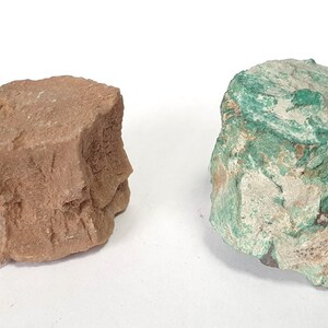 May include: Two rough rocks, one reddish-brown, the other turquoise green. Both have textured, uneven surfaces. They appear to be natural mineral specimens. The rocks are likely to be of geological interest.