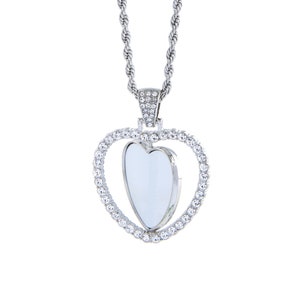 May include: A silver necklace with a heart-shaped pendant. The pendant is surrounded by small clear rhinestones and has a smaller heart-shaped cutout in the centre.