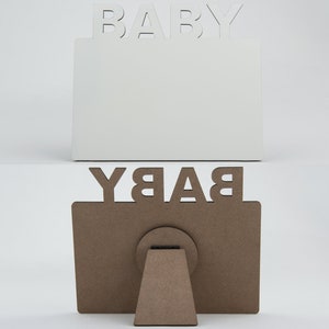 May include: Two wooden picture frames, one white and one brown, with the word "BABY" cut out at the top. The white frame is upright, while the brown frame is displayed with its easel back. The frames are designed for baby photos.