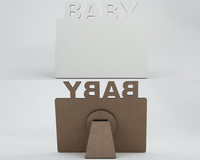 May include: Two wooden picture frames, one white and one brown, with the word "BABY" cut out at the top. The white frame is upright, while the brown frame is displayed with its easel back. The frames are designed for baby photos.