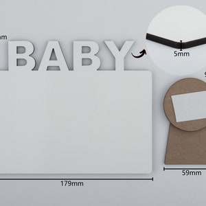 May include: A white rectangular photo frame with the word "BABY" in white letters at the top. The frame is 179mm wide and 149mm tall. A round stand is attached to the back, 59mm wide and 96mm tall.
