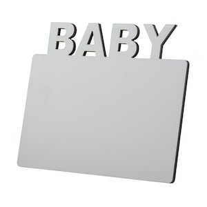May include: A white rectangular sign with the word "BABY" in capital letters at the top. The sign has a black border and is angled slightly towards the viewer, set against a white background.