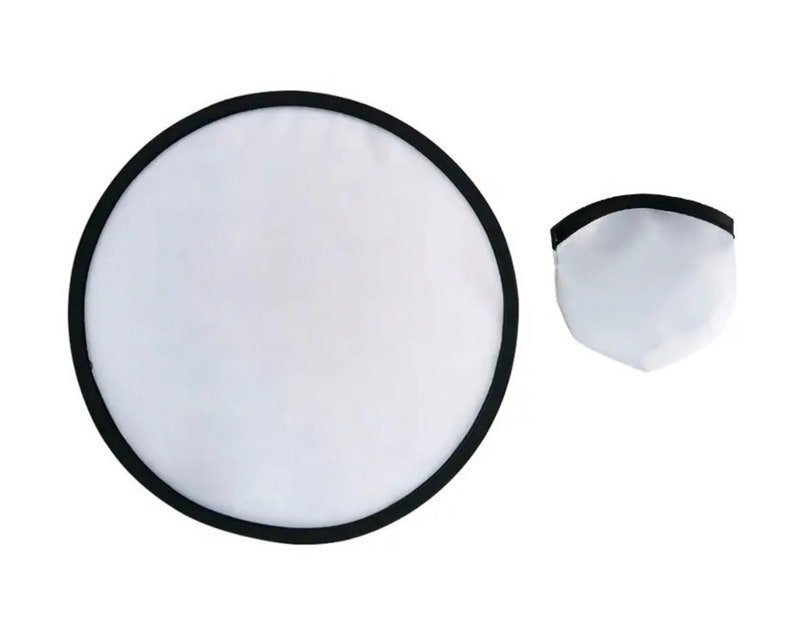 May include: A white and black photography reflector, circular when open and folded into a smaller, triangular shape. The reflector has a black border and is designed to bounce light.