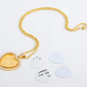 May include: A gold chain necklace with a heart-shaped pendant. The pendant is clear and has a diamond-like design. The necklace is on a white background.