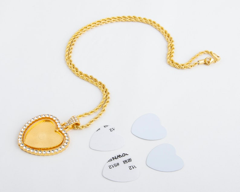 May include: A gold chain necklace with a heart-shaped pendant. The pendant is clear and has a diamond-like design. The necklace is on a white background.