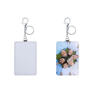 May include: Two white leather keychains with silver key rings. One keychain has a blank white surface and the other has a photo of a family of six smiling and lying on their backs on a grassy lawn.