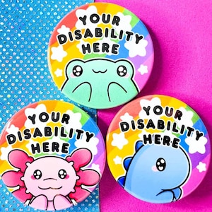 Può includere: Tre bottoni rotondi con sfondi arcobaleno e stelle bianche. Ogni bottone presenta un animale dei cartoni animati diverso: una rana, un axolotl e un dinosauro. Il testo su ogni bottone recita "Your Disability Here".