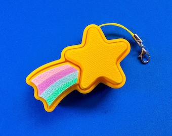 May include: A yellow star-shaped charm with a rainbow-colored comet tail. The charm has a textured surface and a yellow cord with a silver clasp. The background is a solid blue.