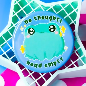 May include: A blue and green button with a cartoon frog and the text "no thoughts head empty".