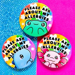 Può includere: Tre spille da balia colorate con sfondi arcobaleno e animali dei cartoni animati. Ogni spilla dice "Per favore, chiedi delle mie allergie".