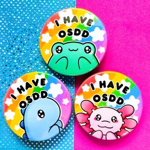 May include: Three colorful button pins with rainbow backgrounds and cartoon animals. Each pin says "I have OSDD" in black text.