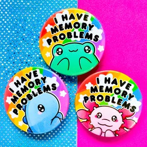 May include: Three colourful button badges with a rainbow background and a white cloud. Each badge features a different cartoon animal and the text "I have memory problems".