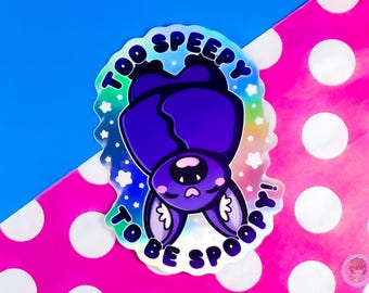 May include: A holographic sticker featuring a cartoon bat hanging upside down. The bat is purple with large ears and a cute face. Text around the bat reads "Too Speepy to be Spoop". The background is blue and pink.