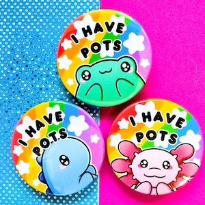 Pode incluir: Três botões redondos e coloridos com o texto "I HAVE POTS" em preto. Cada botão apresenta um animal de desenho animado diferente: um sapo verde, uma baleia azul e um axolotl rosa. O fundo é um design de arco-íris.
