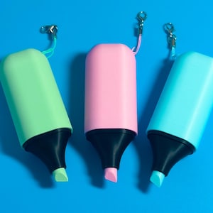 Könnte beinhalten: Drei Schlüsselanhänger in Form von Textmarkern in Hellgrün, Pastellrosa und Hellblau. Jeder Artikel verfügt über eine schwarze Kunststoffspitze, eine farblich passende Kappe und einen kleinen Metallkarabiner an einer Kordel zum Aufhängen.