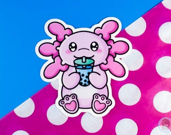 May include: A pink axolotl cartoon sticker with big eyes and a pink and blue bubble tea cup. The sticker is on a pink and white polka dot background.