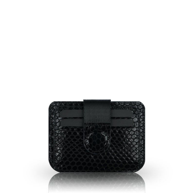May include: Black leather card holder with a crocodile embossed pattern and a black elastic band.
