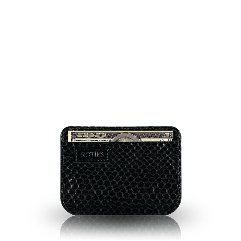 May include: A black leather wallet with a textured surface and a single bill of US currency sticking out of the top. The wallet has the word "ROTIKS" embossed on the front.