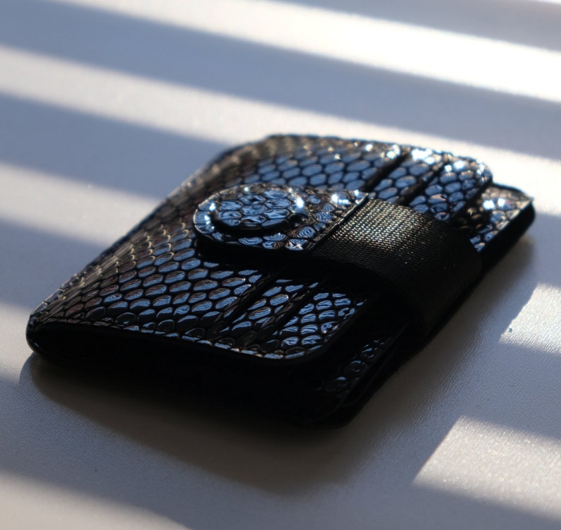 May include: A black leather wallet with a textured snakeskin pattern and a black strap closure.