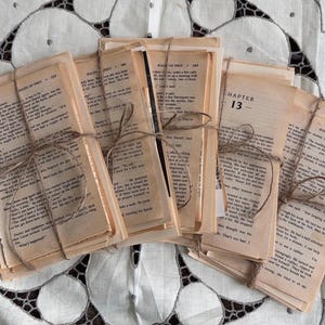 Könnte beinhalten: Mehrere Bündel gealterter Buchseiten, mit Bindfaden zusammengebunden. Die Seiten sind vergilbt und mit Text bedruckt. Die Bündel sind auf einer weißen Oberfläche mit einem Muster angeordnet. Der Text auf den Seiten ist lesbar.