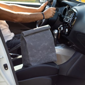 May include: A gray fabric lunch bag sits on the passenger seat of a white car.